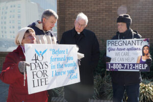Sherry Bramer displayed a sign during the Lenten 40 Days for Life vigil last year. She prayed the rosary during one of her shifts along with Ed Harpring, center, and Archbishop Joseph E. Kurtz. 40 Days for Life holds vigils in the fall and Lent each year outside the EMW Women’s Surgical Center. The fall vigil has begun and parishioners are urged to sign up for a shift. (Record File Photo by Marnie McAllister) 